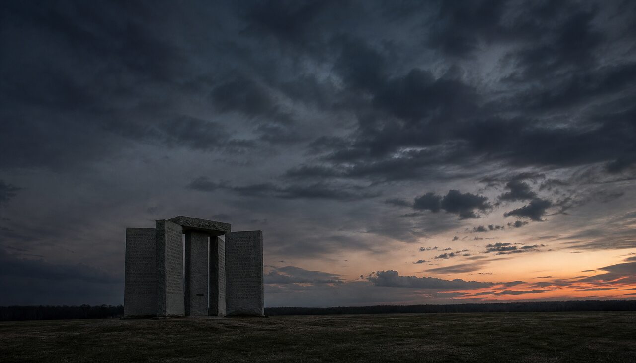 The four slabs alone in a field at dusk, recommending the removal of most of the people who would ever come to read them.