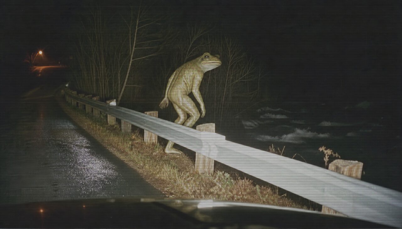 A bipedal frog-faced figure caught in patrol headlights, one webbed foot already over the guardrail above the Little Miami River.