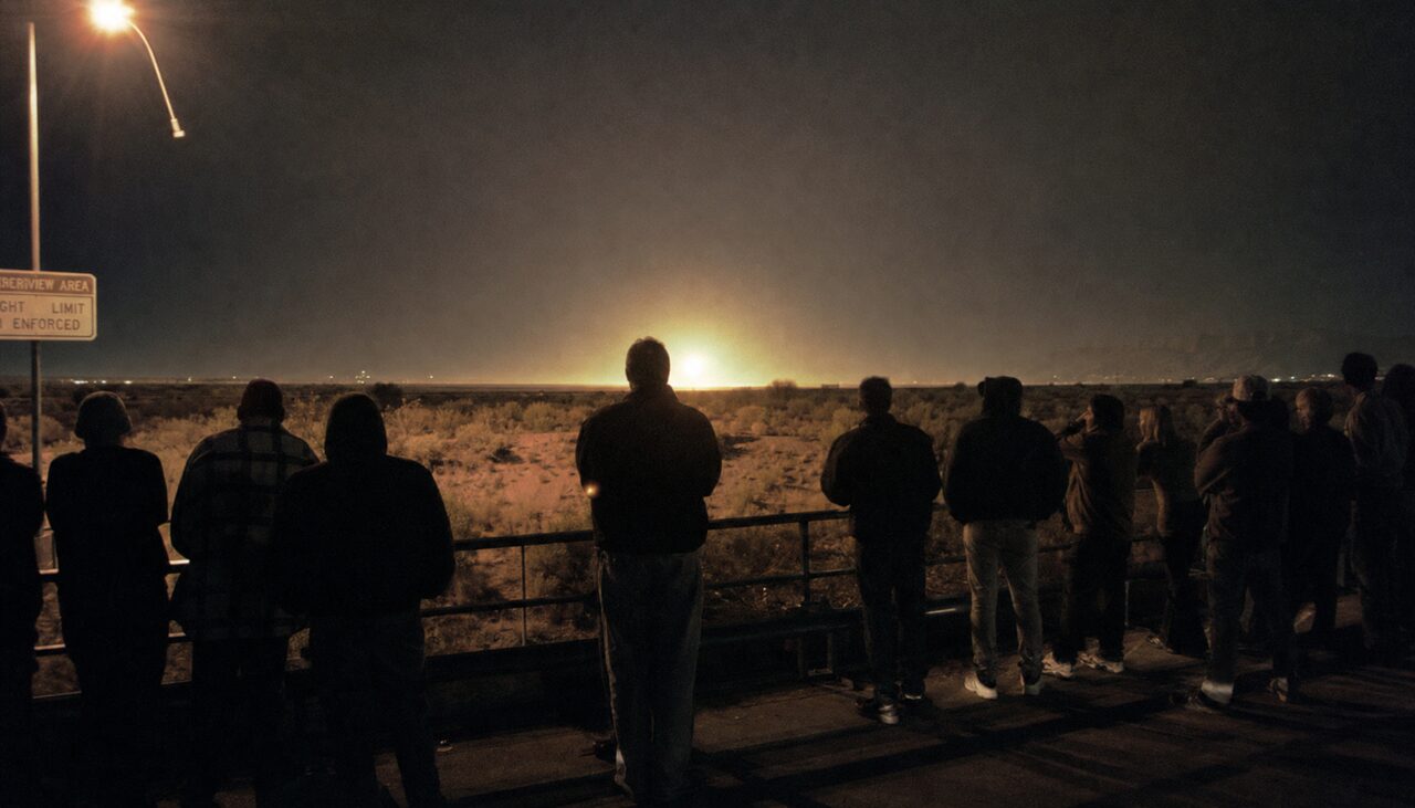 Every night they still come, line up at the railing, and wait for the flat to produce a light. Most of them know by now what it probably is. They watch it anyway.