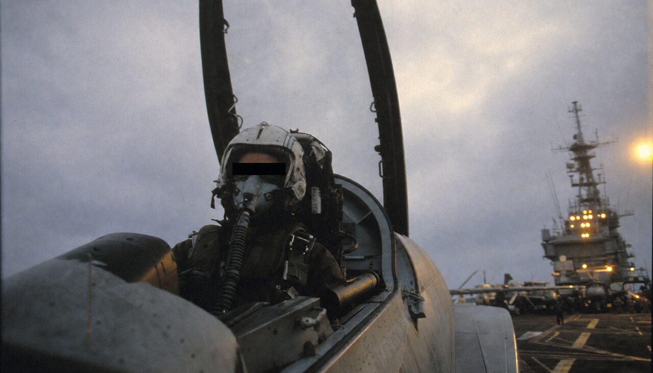 A naval aviator in flight gear and oxygen mask in an F/A-18 cockpit, identifying details obscured.