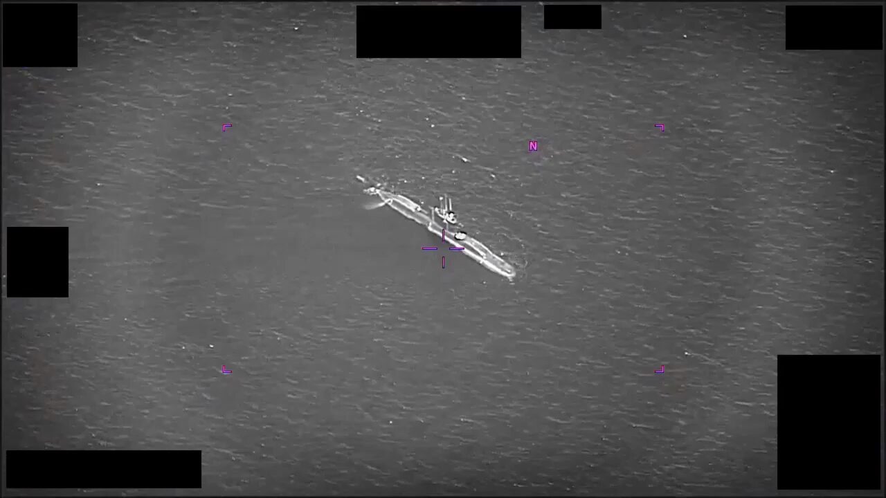A frame from the declassified footage: objects tracked near a submarine on the surface, entering and leaving the water.