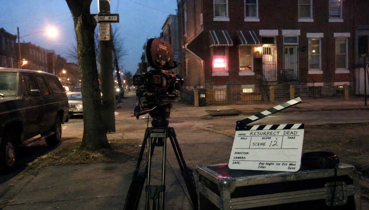 A documentary crew on a quiet residential block. Scene 12, by the slate.